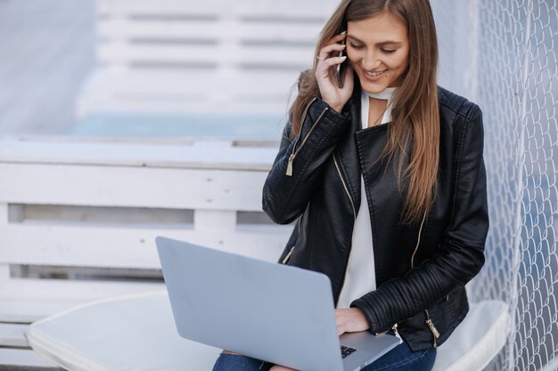 A mulher de sorriso senta-se em um banco branco falando em seu telefone