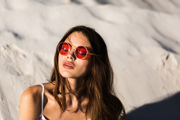 A mulher em óculos de sol vermelhos encontra-se numa praia branca