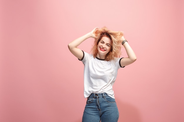 A mulher feliz que está e que sorri contra a parede cor-de-rosa.