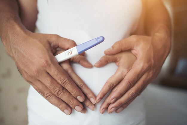 A mulher gravida e seu marido entregam mostrar a forma do coração.