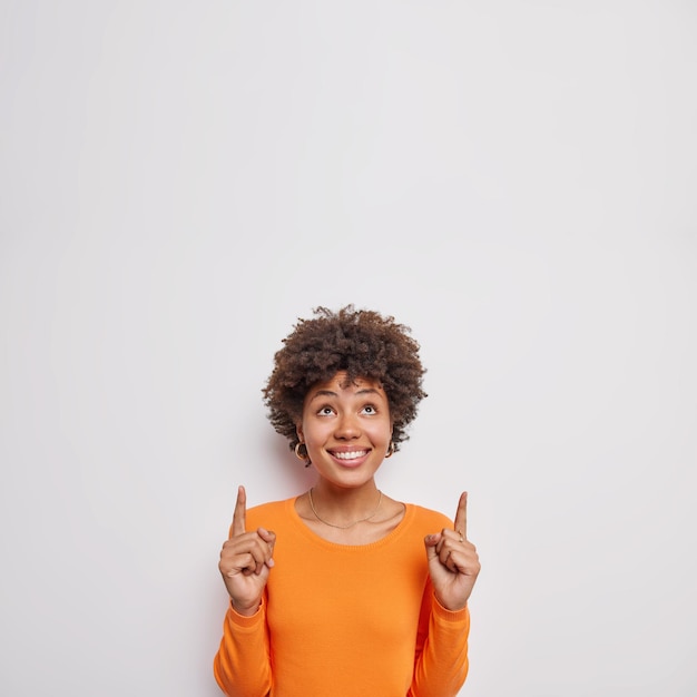 A mulher indicada acima com os dois dedos indicadores usa um macacão laranja casual atrai sua atenção para uma oferta bacana isolada sobre o fundo branco mostra o logotipo