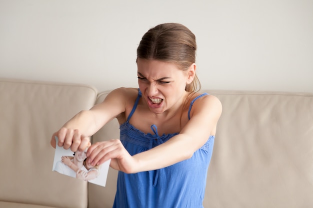 Foto grátis a mulher irritada rasga a fotografia de papel em duas partes