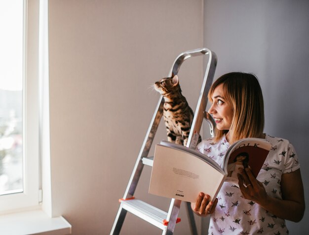 A mulher lê um livro enquanto o gato de Bengala está na escada atrás dela