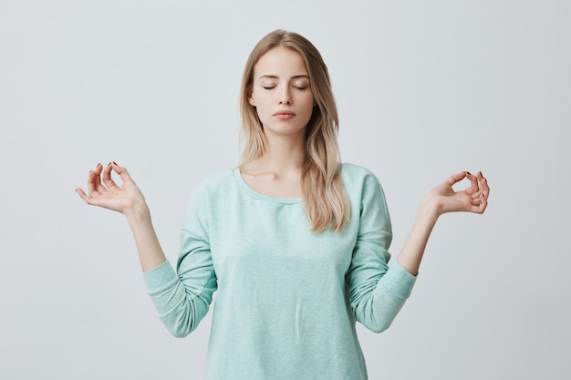 A mulher loira tranquila e tranquila se sente relaxada, fica em posição de lótus, tenta se concentrar ou se concentrar, fecha os olhos, goza de silêncio, tenta encontrar o equilíbrio. Atmosfera calma e meditação