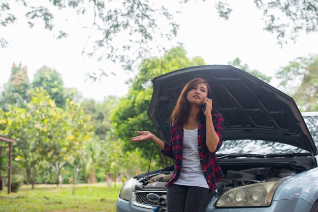 A mulher nova com carro quebra para baixo e está chamando os serviços de emergência.