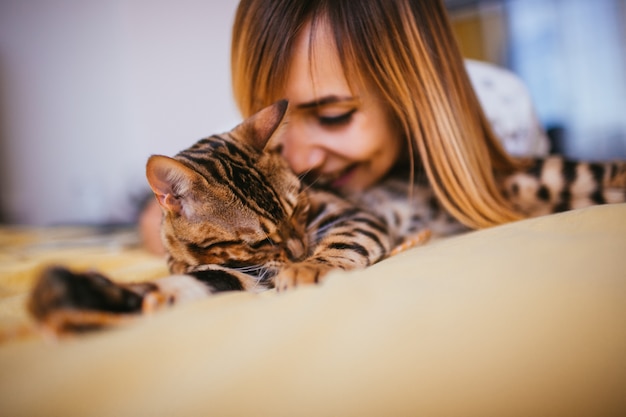 A mulher se inclina para o gato de Bengala enquanto fica na cama