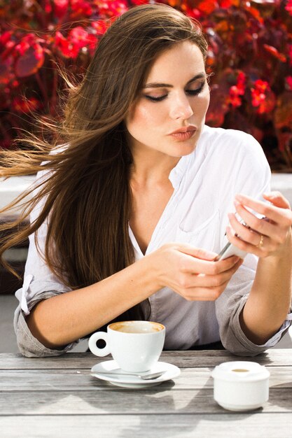 A mulher segura um smartphone sentado à mesa