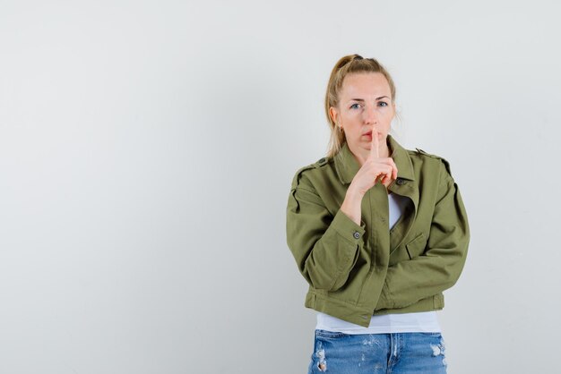 A mulher séria está mostrando um gesto silencioso, colocando o dedo indicador nos lábios no fundo branco