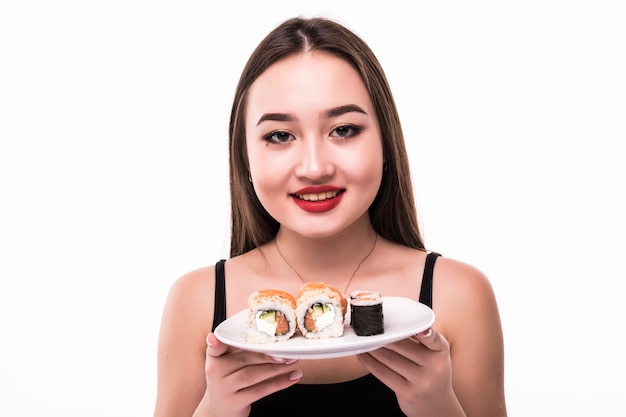 A mulher sorridente com cabelo preto e lábios vermelhos prova rolos de suushi com pauzinhos de madeira na mão