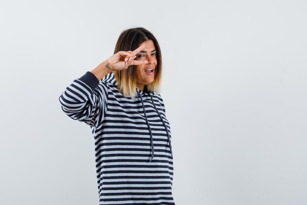 A mulher sorridente está segurando os dedos perto do olho no fundo branco