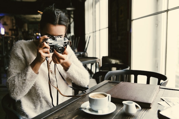 A mulher tira uma foto na fotocamara retro, sentada no café