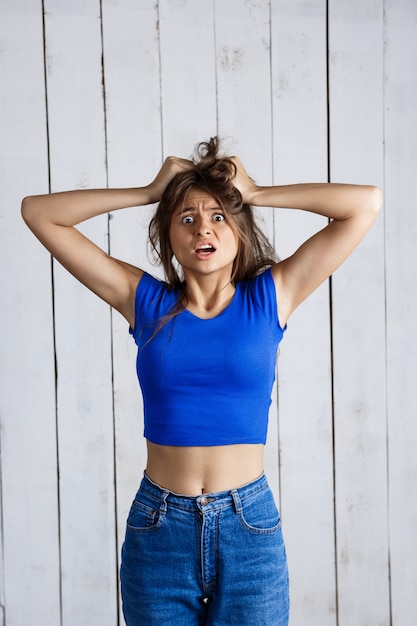 Foto grátis a mulher virada que guarda o cabelo cede a parede de madeira branca.