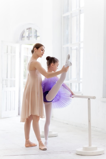 A pequena bailarina posando no bar de ballet com o professor pessoal no estúdio de dança