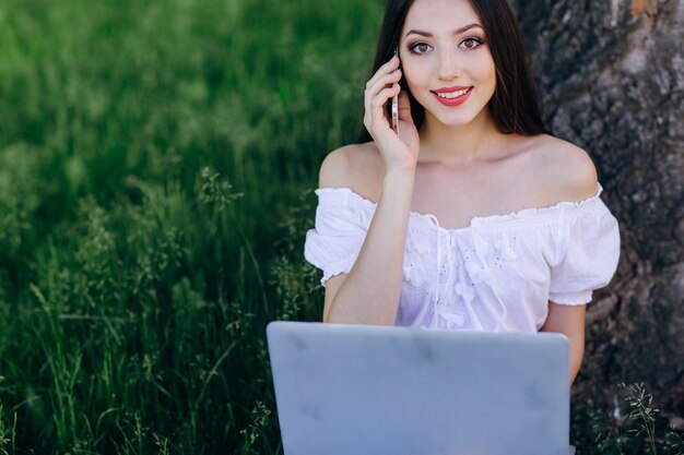 A rapariga sentada contra uma árvore falando ao telefone