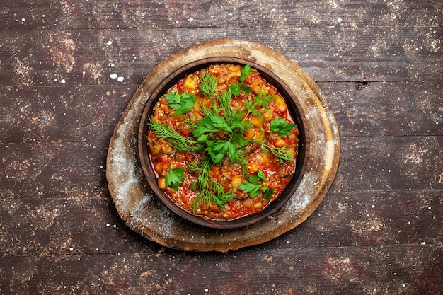 A saborosa refeição cozinhada da vista superior consiste em vegetais fatiados e verduras em uma refeição rústica marrom com molho