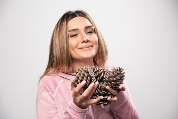 A senhora loira em um moletom rosa faz uma cara positiva e feliz segurando cones de carvalho.