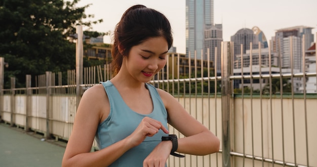 A senhora nova do atleta de Ásia exercita a verificação do progresso que olha o monitor da frequência cardíaca no smartwatch na cidade urbana. Corredor de menina adolescente descansando exausto após treino de corrida intenso cardio de treino.