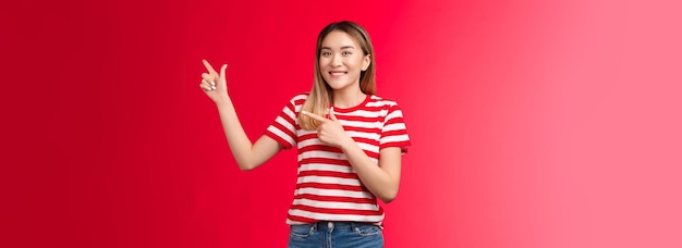 Foto grátis a simpática e alegre jovem loira coreana apontando para o canto superior esquerdo sugere pla perfeito