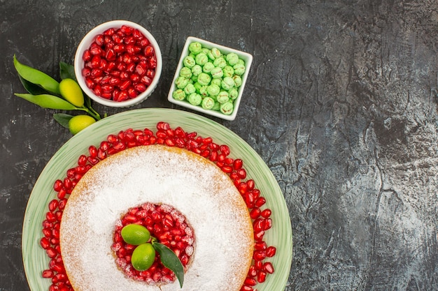 A vista de cima em close-up doces um bolo com frutas cítricas taças de doces verdes e sementes de romã