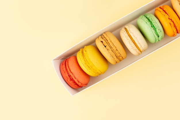 A vista de cima macarons franceses alinhados na mesa amarela bolo biscoito açúcar doce