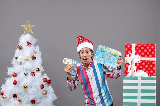 A vista frontal surpreendeu o homem com um chapéu de papai noel com mola espiral segurando um mapa-múndi e um bilhete de viagem