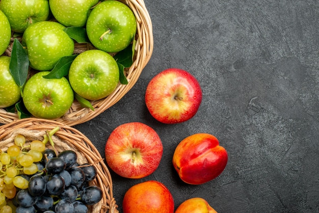 A visualização em close-up de cima frutifica as apetitosas maçãs e os cachos de uvas na cesta e nectarinas