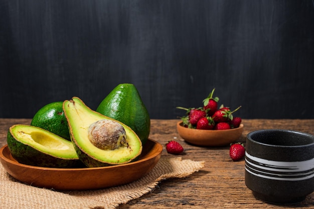 Abacate e morango na velha mesa de madeira halfs na tigela de madeira e serapilheira frutas comida saudável