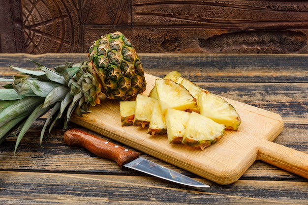 Abacaxi fatiado em uma placa de corte com uma vista lateral de faca de fruta em uma superfície de madeira grunge e telha de pedra