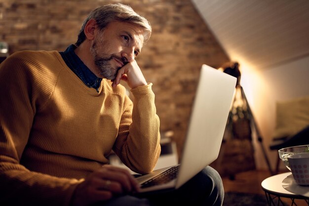 Abaixo vista do empresário pensativo usando laptop à noite em casa