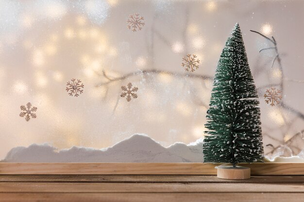 Abeto de ornamento na mesa de madeira perto do banco de neve, galho de planta, flocos de neve e luzes de fada