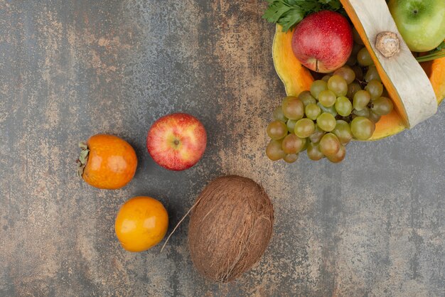 Abóbora com maçãs, coco e uvas na parede de mármore