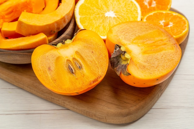 Abóbora de abóbora em tigelas corta caqui, mandarinas e laranjas na tábua de cortar na mesa branca