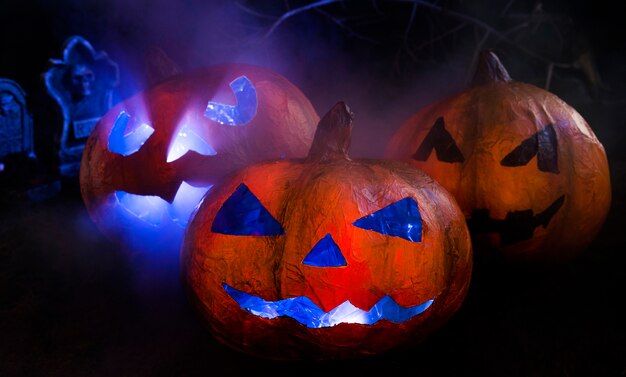 Abóboras artesanais de Halloween com rostos iluminados esculpidos e lápides para trás