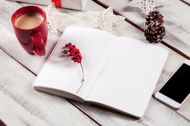 Abra o caderno na mesa de madeira com um telefone e as decorações de Natal.
