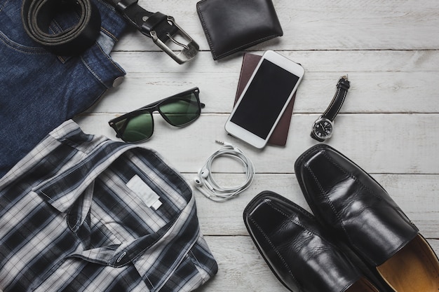 Acessórios de vista superior para viajar com o conceito de vestuário do homem. camisa, jean, telefone móvel em fundo de madeira. Vestuário, óculos de sol e sapatos na mesa de madeira.