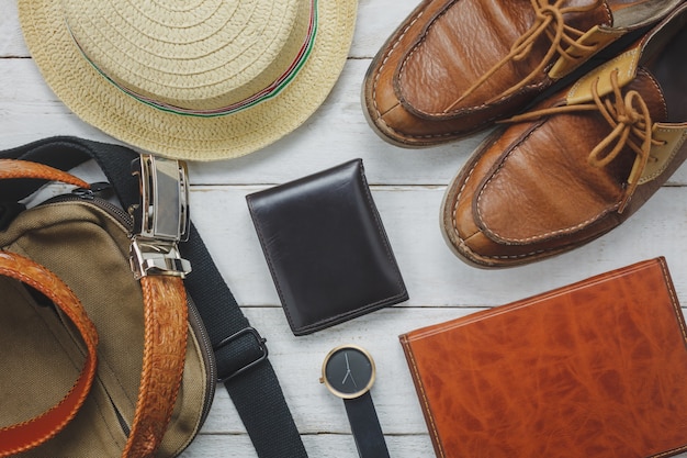 Acessórios de vista superior para viajar com o conceito de vestuário do homem. Carteira em fundo de madeira. Revestimento, bolsa, chapéu, caderno e sapato na mesa de madeira branca.