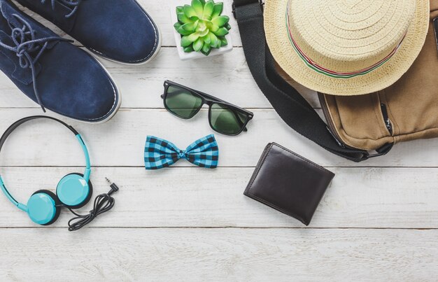 Acessórios de vista superior para viajar com o conceito de vestuário do homem. fone de ouvido no fundo de madeira. gravata, carteira, óculos de sol, sapato, bolsa e chapéu na mesa de madeira.