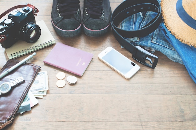 Acessórios do viajante, itens essenciais de férias de homem jovem com passaporte, câmera, dispositivo móvel e bolsa em fundo de madeira com espaço de cópia