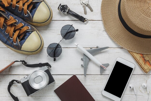 Acessórios para mulheres com vista superior para viajar conceito. Telefone móvel e fone de ouvido em fundo de madeira. Avião, chapéu, passaporte, relógio, óculos de sol na mesa de madeira.