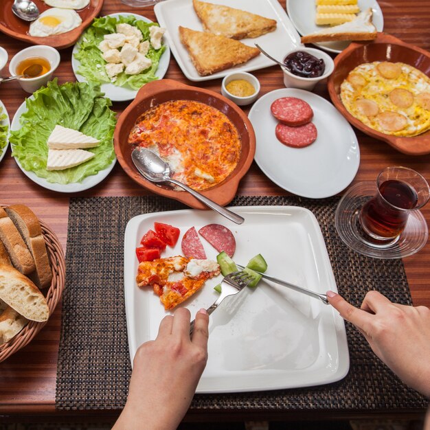 Acima, café da manhã variado com omelete e copo de chá e mão humana em servir guardanapos