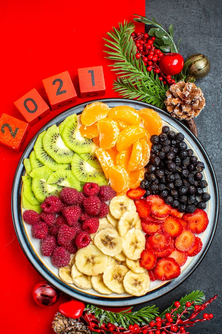 Foto grátis acima, vista da coleção de frutas frescas no prato de jantar acessórios de decoração ramos de abeto e números meia de natal em um guardanapo vermelho sobre um fundo preto
