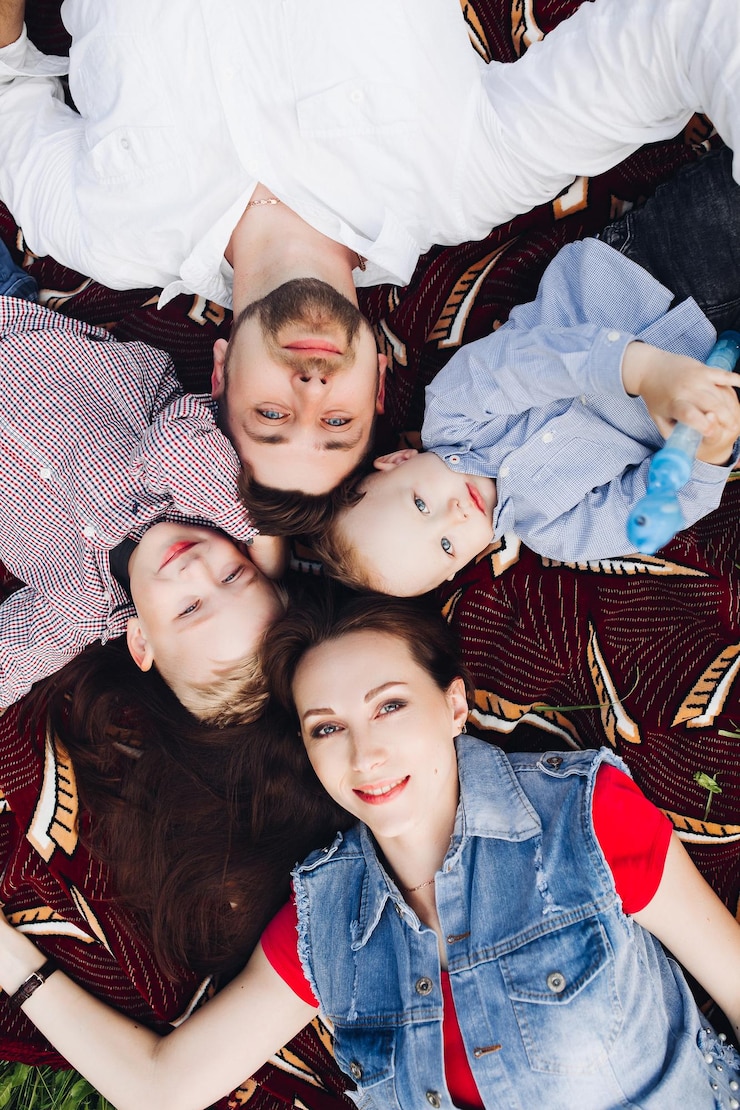 Foto grátis acima vista da família feliz deitada no parque junto com crianças sorrindo brincando olhando para a câmera pais positivos com dois filho posando ao ar livre conceito de família e emoção