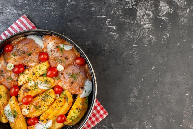 Acima vista da refeição de frango cru picante com batatas legumes em panela na toalha vermelha despojada no lado direito no fundo cinza