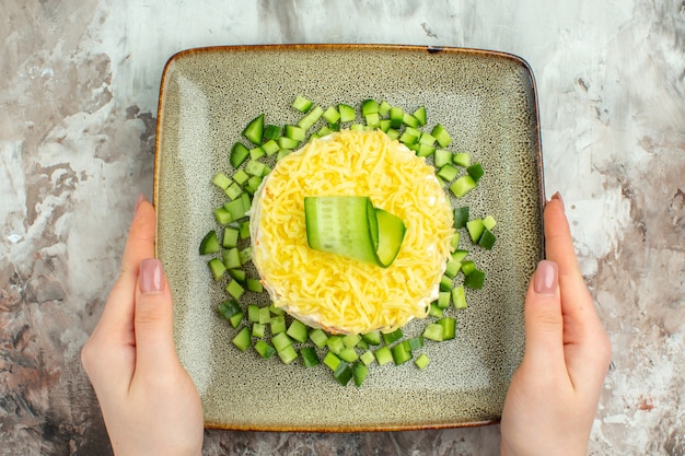 Acima, vista de uma mão segurando uma saborosa salada servida com pepino picado em um fundo de cor mista