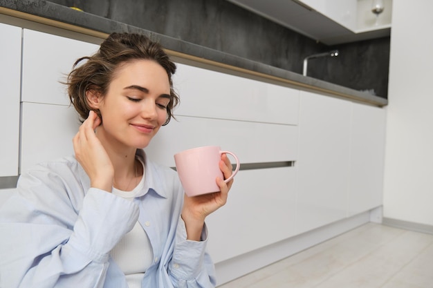 Aconchego e conceito de casa jovem mulher gosta de sua xícara de café da manhã bebe chá fresco e sorri f