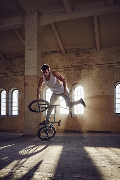 Acrobacias de BMX e salto andando em um parque coberto, luz solar.