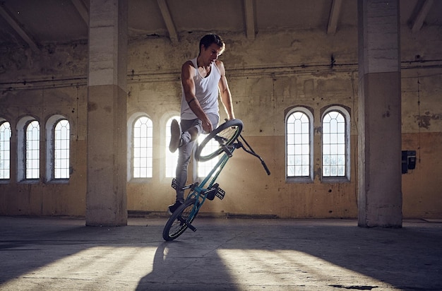 Acrobacias de BMX e salto andando em um parque coberto, luz solar.