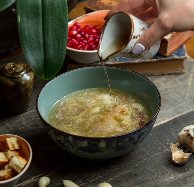 Adicionando caldo na sopa de galinha em uma tigela azul autêntica