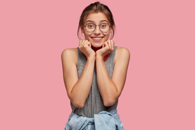 Foto grátis adolescente alegre com um sorriso cheio de dentes, segurando o queixo com as duas mãos e olhando com uma expressão feliz diretamente para a câmera