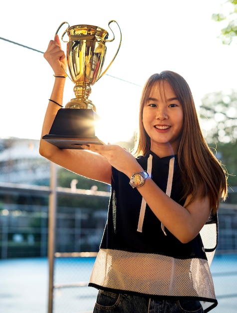 Adolescente asiática em roupas esportivas segurando um troféu ao ar livre